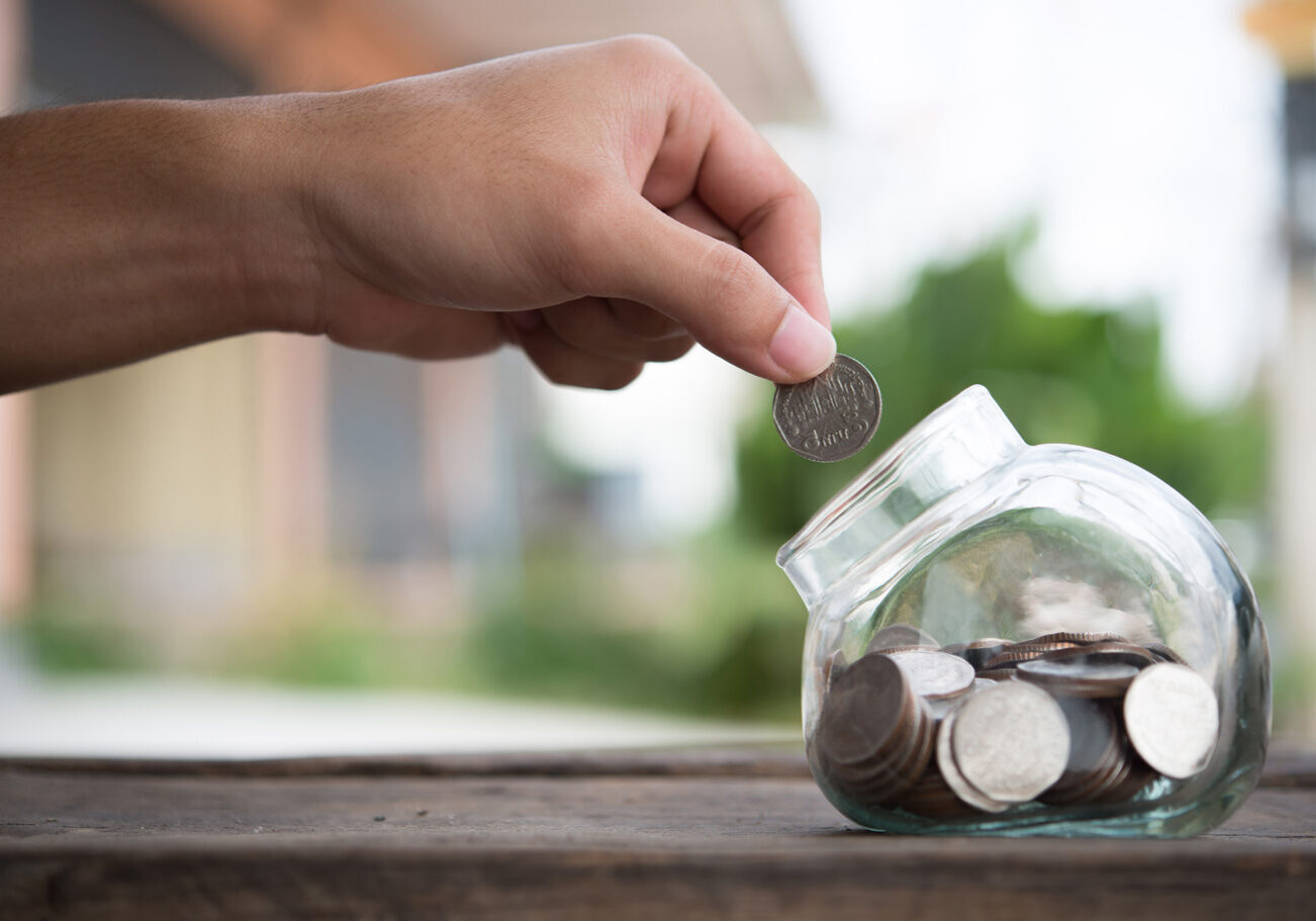 Man hands saving money into bottle for cash in future investment.