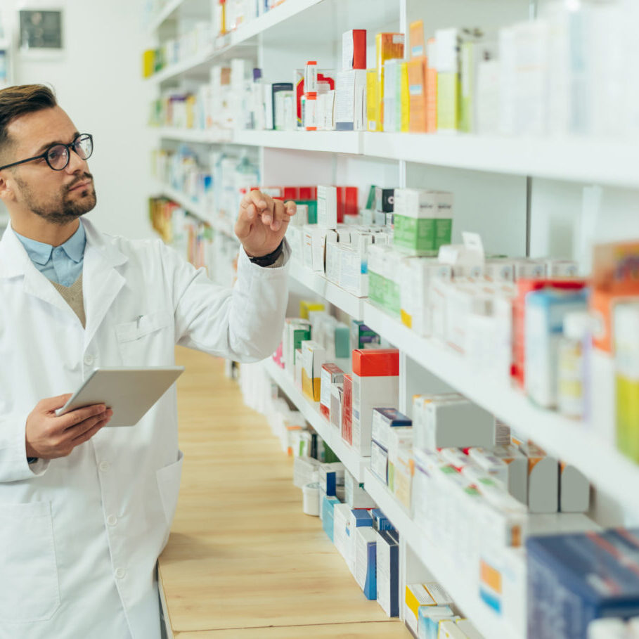 Portrait of a handsome pharmacist working in a pharmacy while checking medications on the shelf